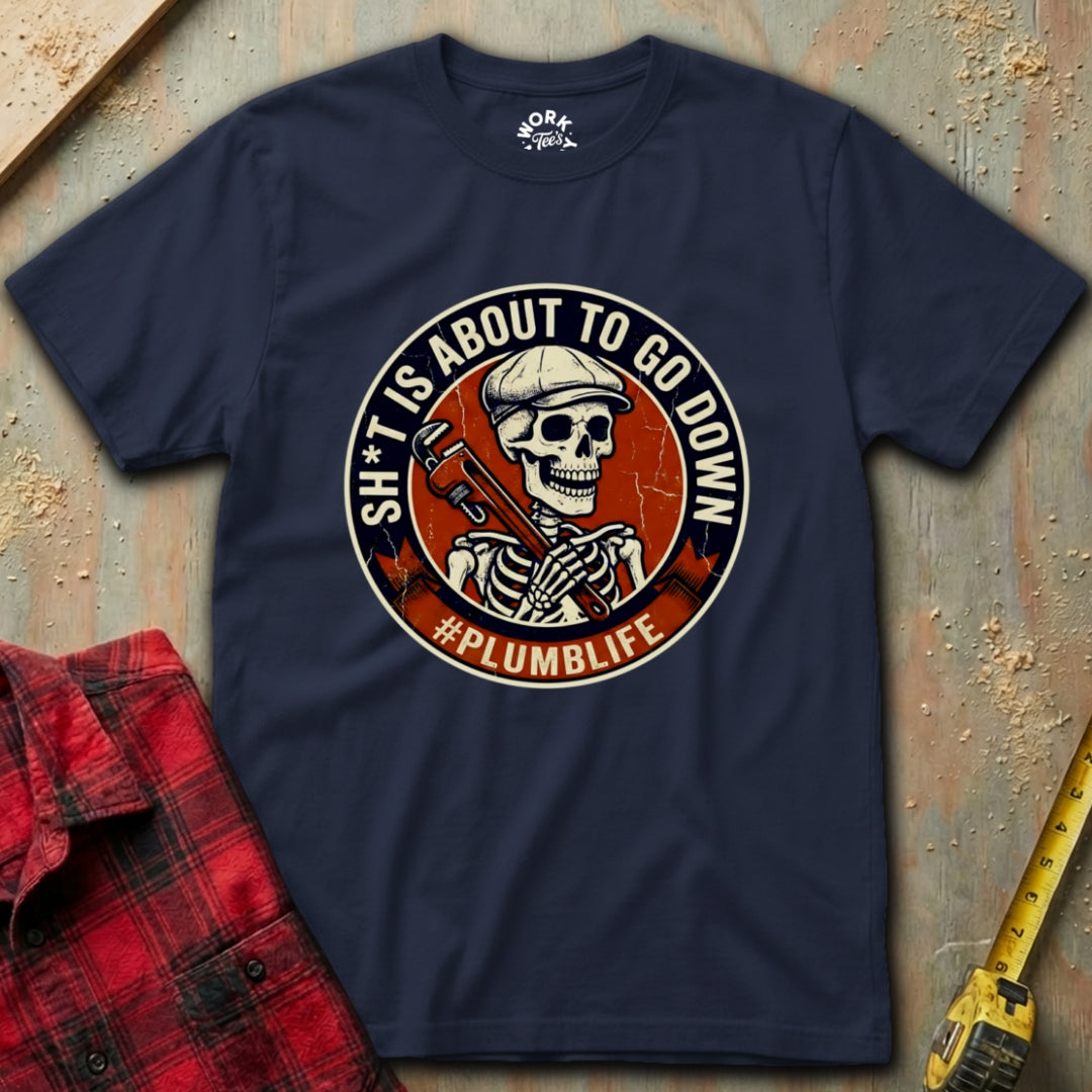 Navy blue t-shirt with a graphic design featuring a skeleton and text, placed on a textured surface with a red flannel shirt and yellow tool in the background.