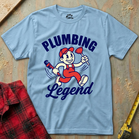 Light blue t-shirt with 'Plumbing Legend' graphic on a wooden surface with tools.