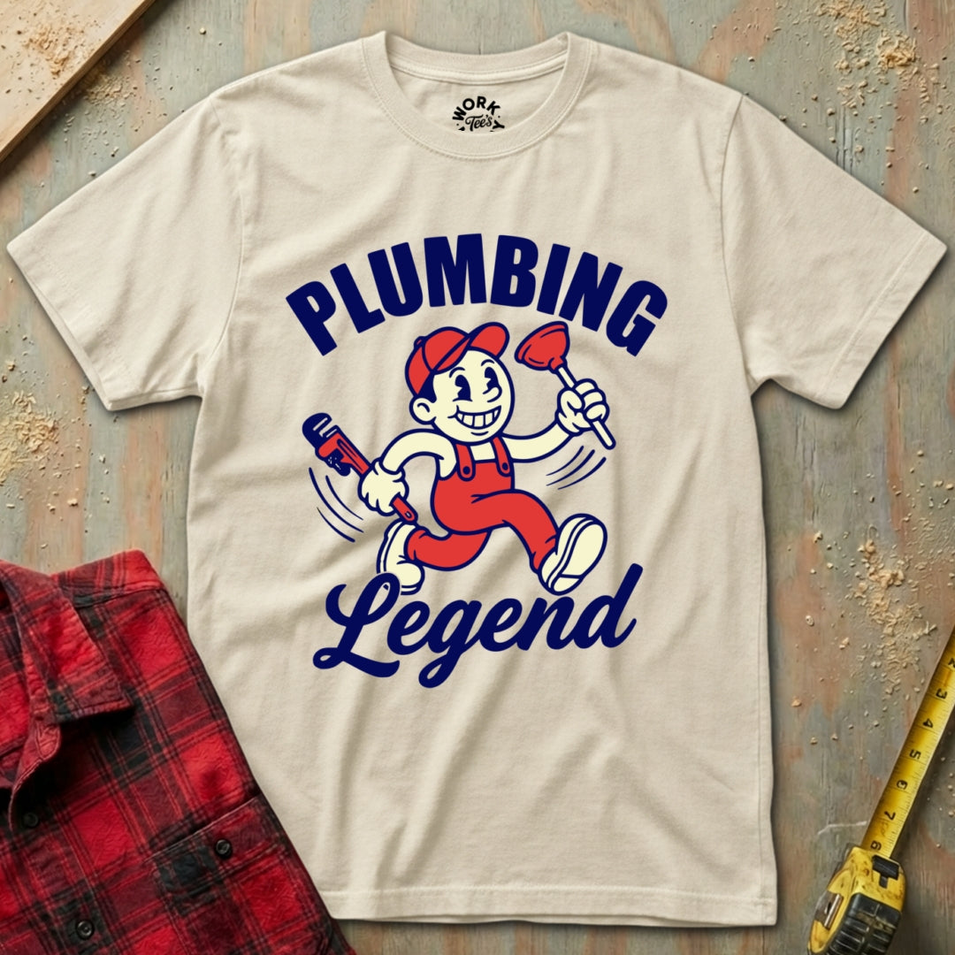 Beige t-shirt with 'Plumbing Legend' graphic design on a textured surface with tools.