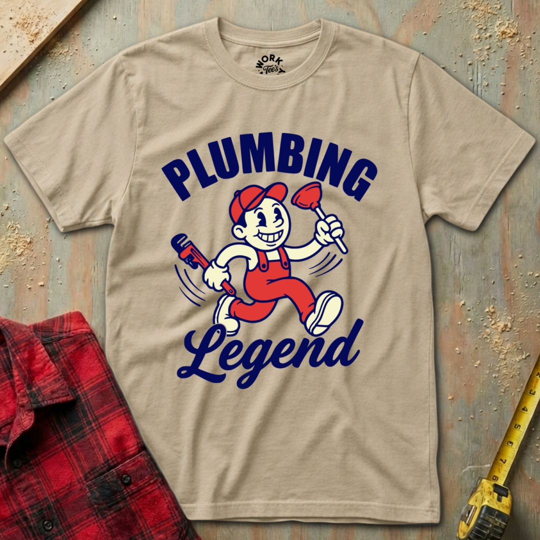 Beige t-shirt with 'Plumbing Legend' graphic on a wooden surface with tools.