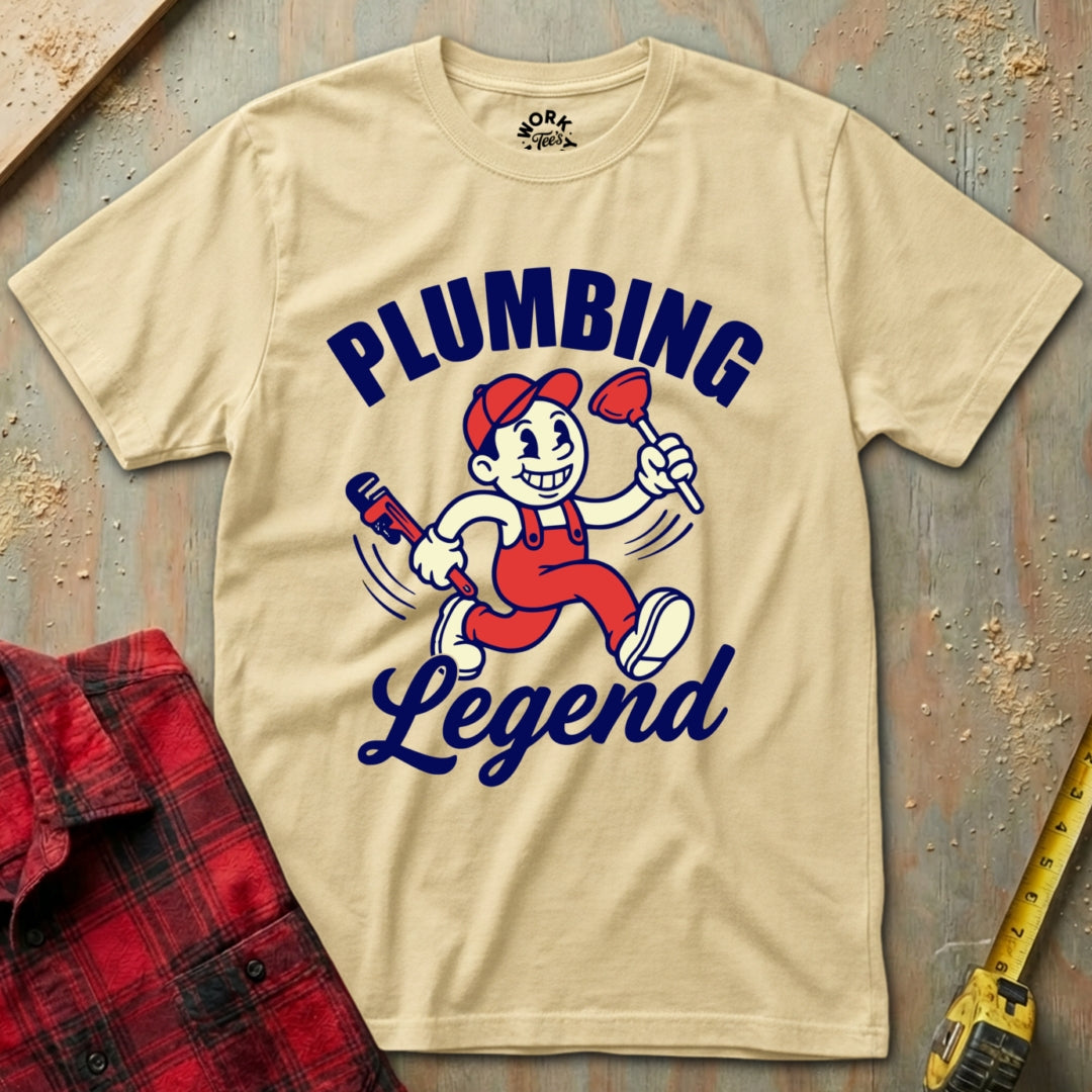 Beige t-shirt with 'Plumbing Legend' graphic on a textured surface with tools.