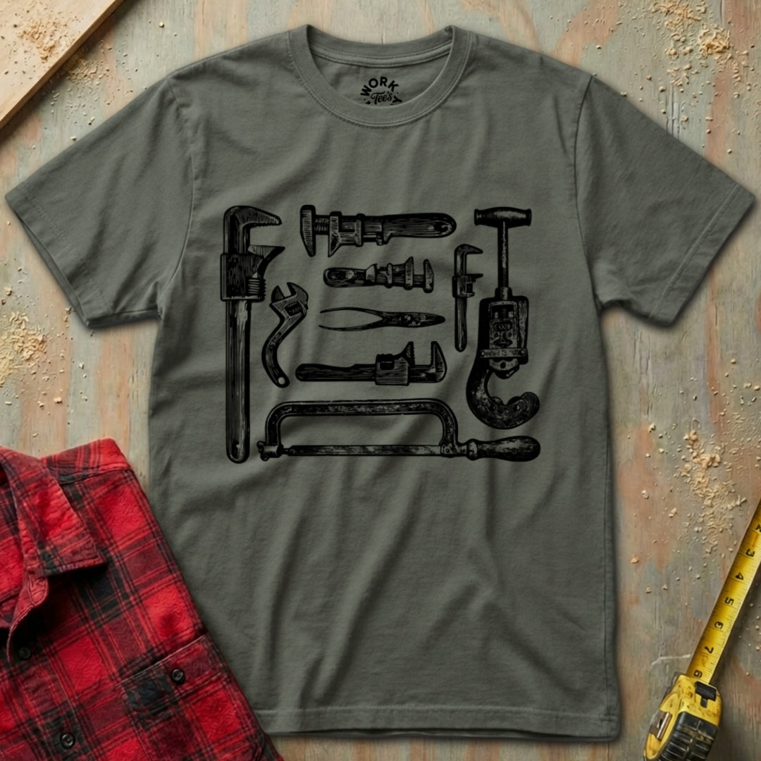Gray t-shirt with black tool graphic on a textured surface with a red flannel shirt and yellow tape measure.