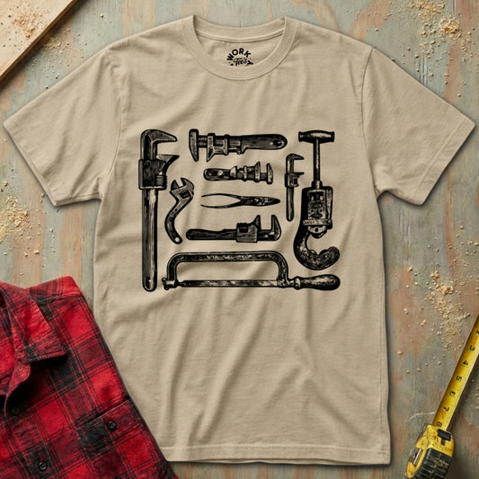 Beige t-shirt with black tool graphic on a textured surface with plaid shirt and tape measure.