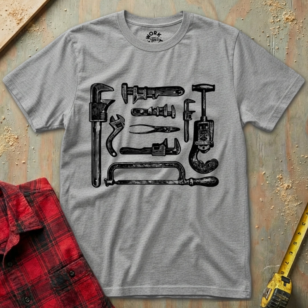 Gray t-shirt with black tool graphic on a textured surface with a red flannel shirt and yellow tape measure.