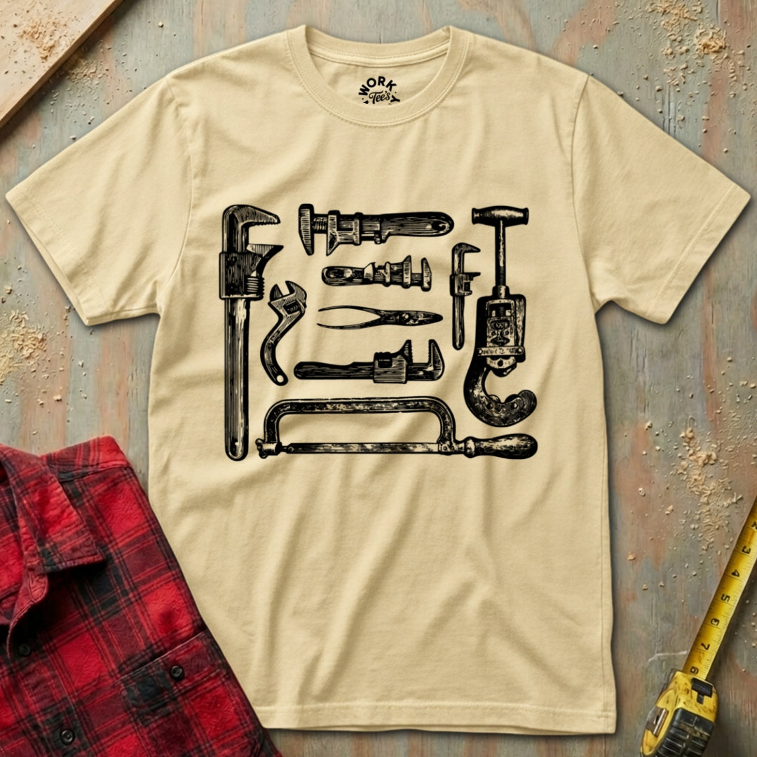 Beige t-shirt with black tool graphic on a rustic wooden surface with plaid shirt and tape measure.