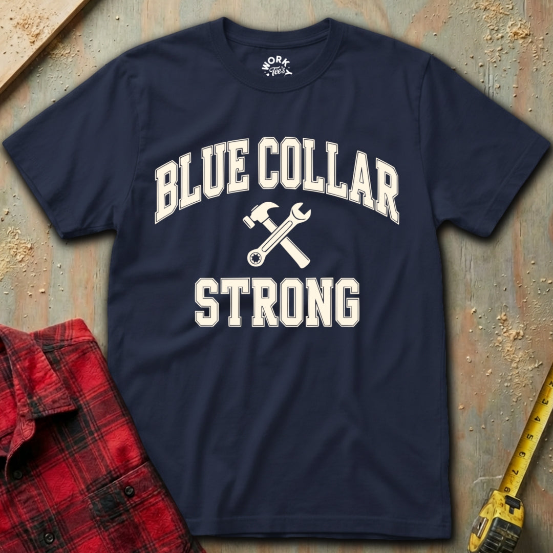 Navy blue t-shirt with 'Blue Collar Strong' text and crossed wrenches on a textured surface with plaid shirt and tape measure.