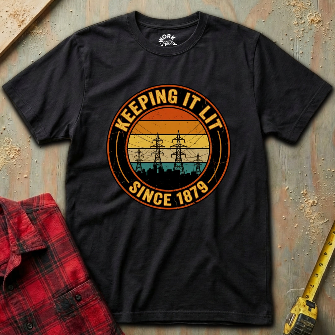 Black t-shirt with a graphic design on a textured surface with a red shirt and yellow tool in the background.