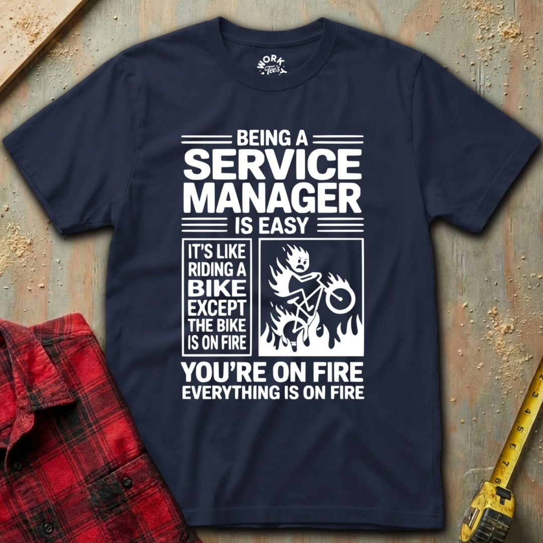 Navy blue t-shirt with humorous text design on a textured surface with a red plaid shirt and yellow tool in the background.