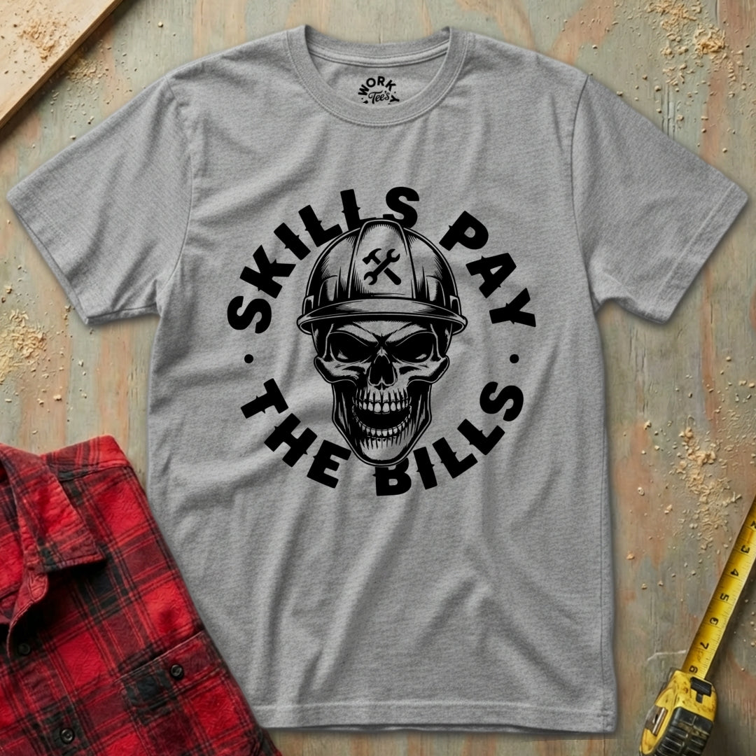 Gray t-shirt with skull graphic and text 'SKILLS PAY THE BILLS' on a textured surface.