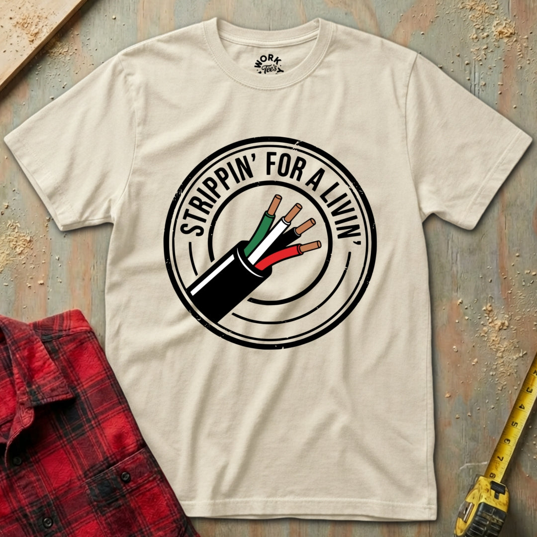 Beige t-shirt with 'Strippin' for a Living' graphic on a textured surface with plaid shirt and tape measure.