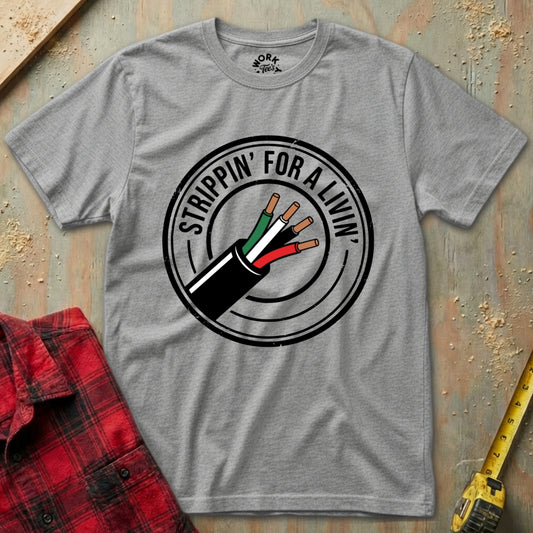 Gray t-shirt with 'Strippin' for a Livin' graphic design on a wooden surface with plaid shirt and tape measure.