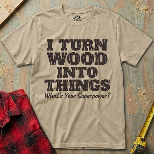 Beige t-shirt with text 'I turn wood into things. What's your superpower?' on a wooden background.