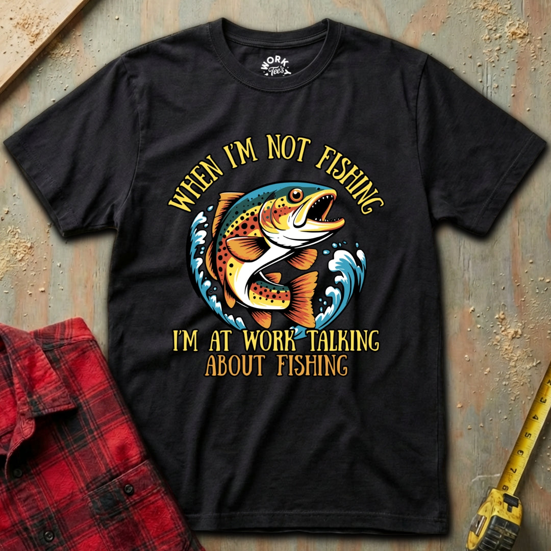 Black t-shirt with fishing graphic and text on a textured surface with plaid shirt and tape measure.