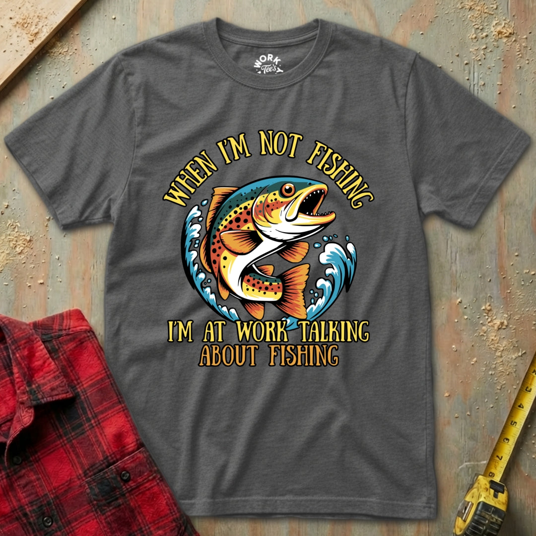 Gray t-shirt with fishing graphic and text on a wooden surface with a red plaid shirt and yellow tool.