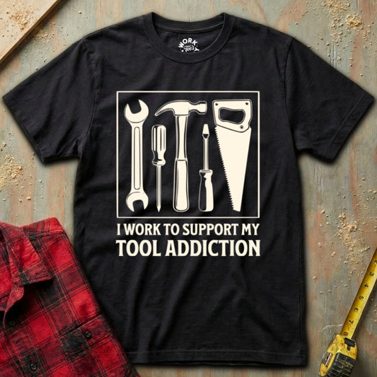 Black t-shirt with tool graphic and text on a textured surface with plaid shirt and tape measure.