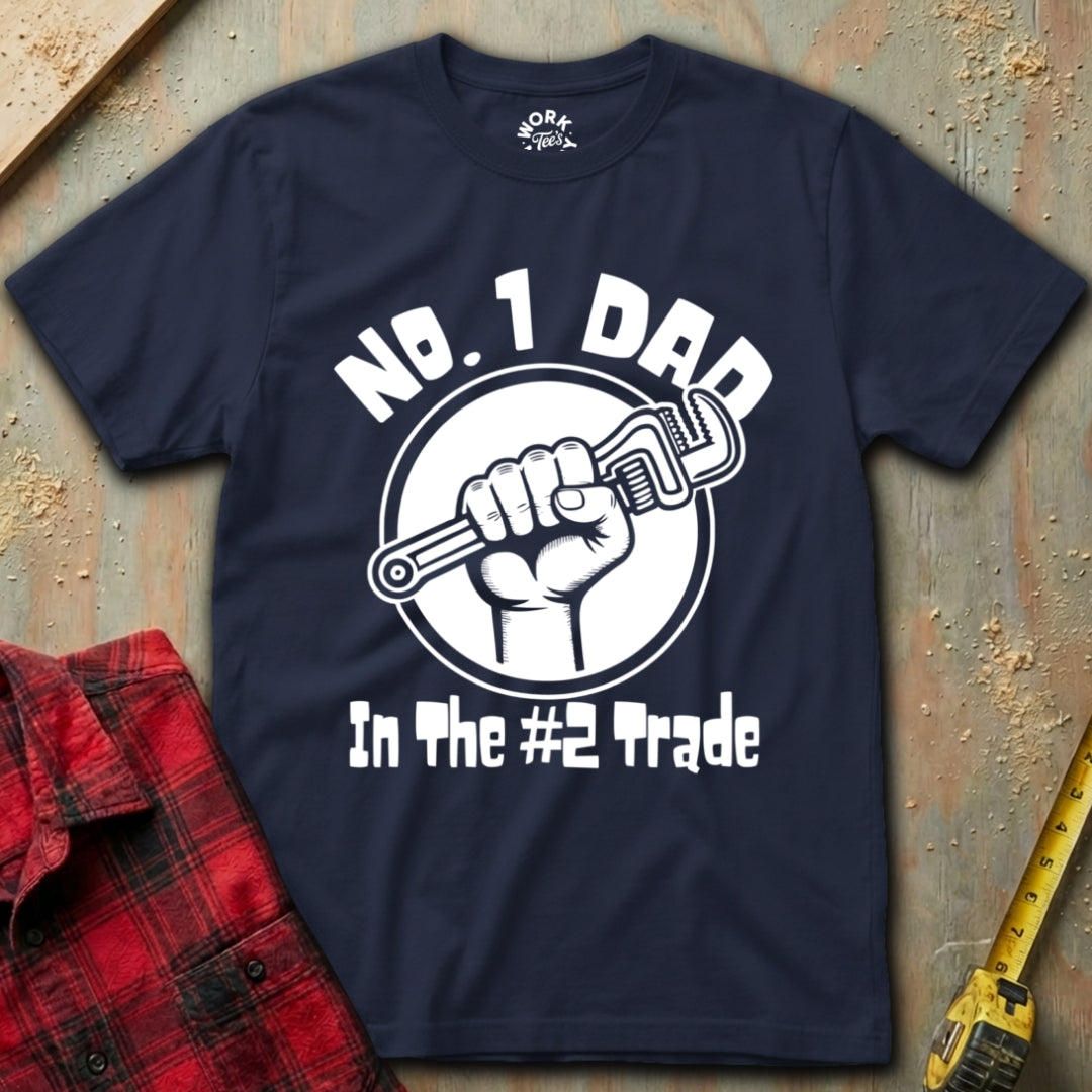 Navy blue t-shirt with 'No. 1 Dad in the #2 Trade' graphic on a textured surface with plaid shirt and tape measure.